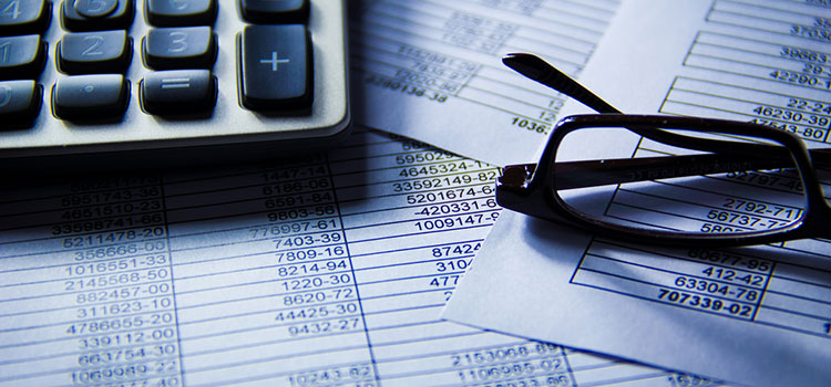 A calculator and pair of reading glasses sitting on top of paperwork.