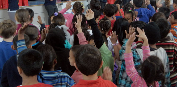 Children raising their hands during a school assembly.