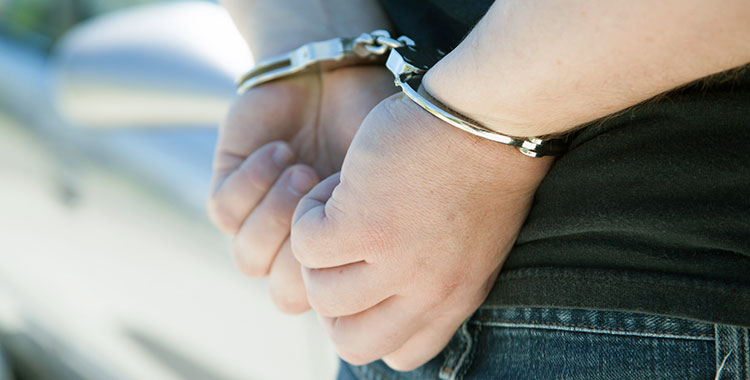 An individual with their hands handcuffed behind their back.