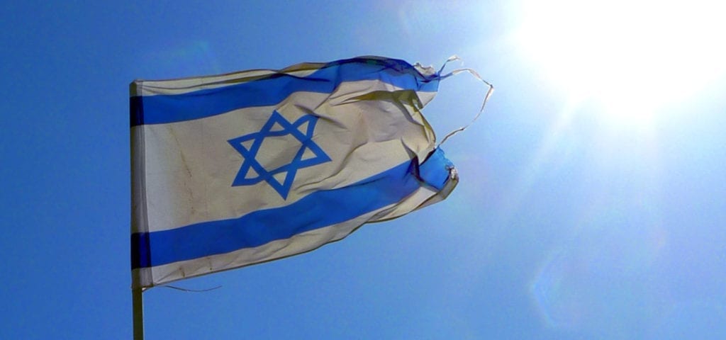 The flag of Israel flies under a sunny, blue sky.