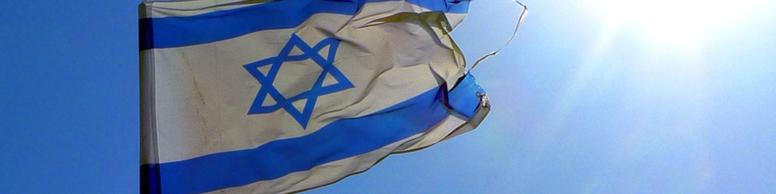 The flag of Israel flies under a sunny, blue sky.