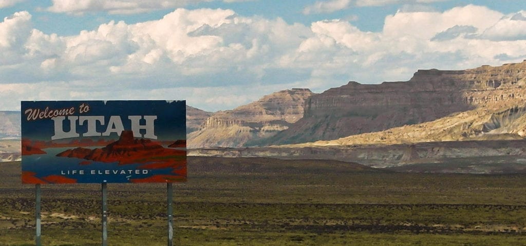 A "Welcome to Utah" sign alongside the highway in the Southwest plains.