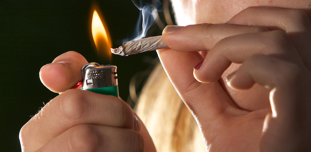 An amateur cannabis smoker lights a hand-rolled joint.