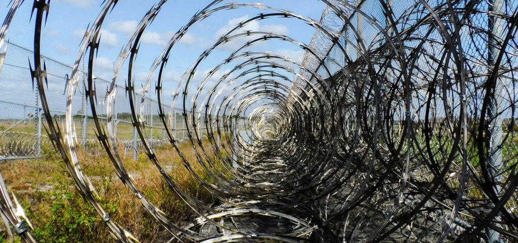 A barbed wire-covered fence outside of a prison facility.