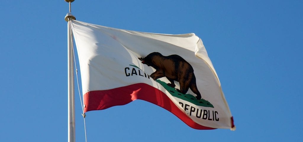 The state flag of California flying on a clear, blue sky day.