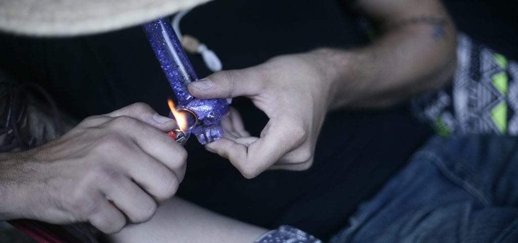 A man uses a lighter and glass pipe to smoke some cannabis.