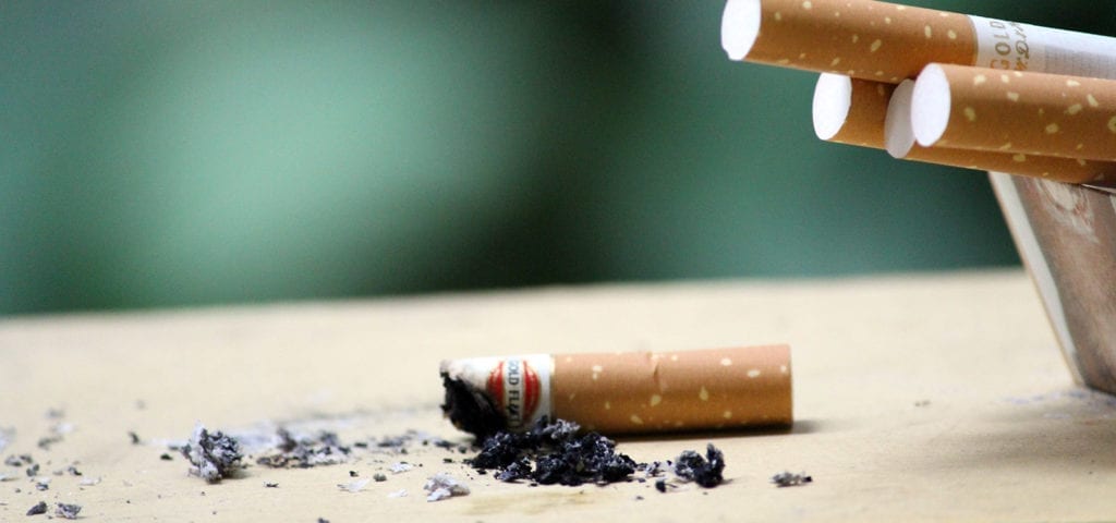 A cigarette butt and several unsmoked cigarettes next to an ashtray.