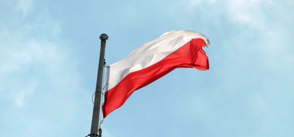 The flag of Poland flying in front of the blue sky.