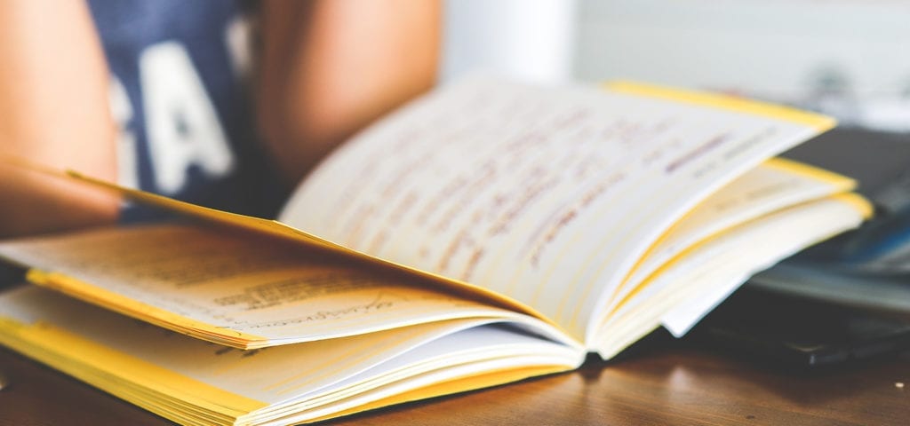 A student reads her notebook at a classroom desk.