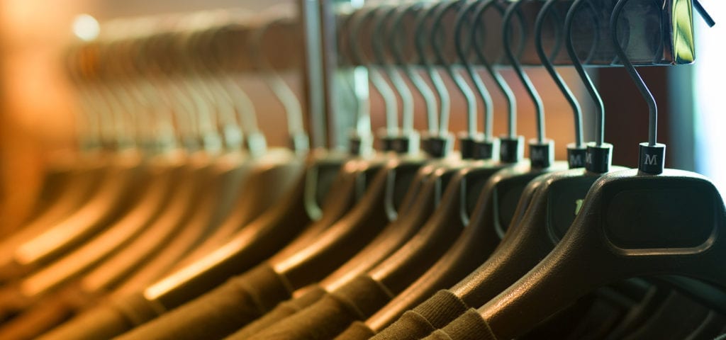 A t-shirt hanger lined with black Ts inside of a retailer location.