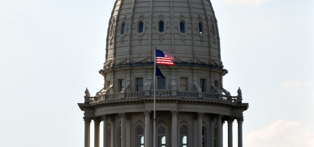 The American flag and Michigan state flag flying in front of the Michigan Capitol Building's dome in Lansing, MI.