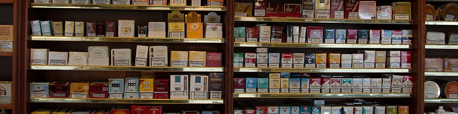 A wall of tobacco products inside of a smoke shop selling cigarettes, cigars, and rolling tobacco.