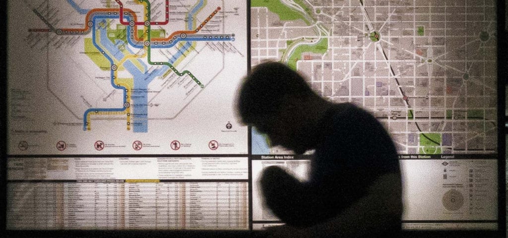 A man's silhouette hunched over in front of a Washington DC metro map.