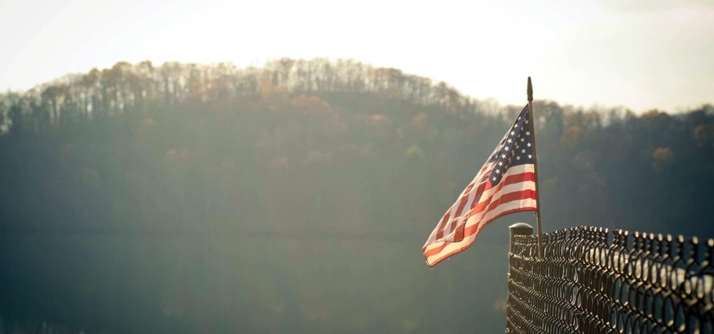 The flag of the United States of America flying on a dock next to still water.