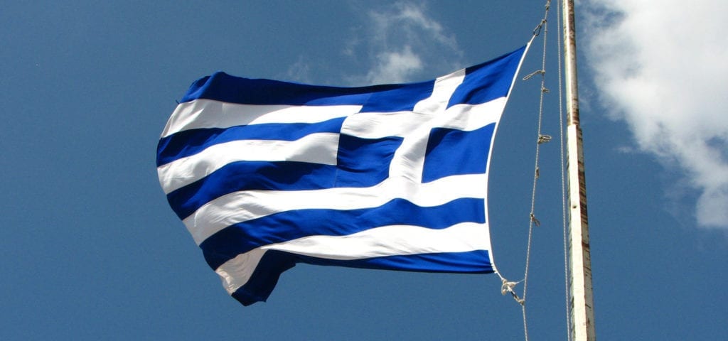 The flag of Greece being blown by wind from the Mediterranean Sea.