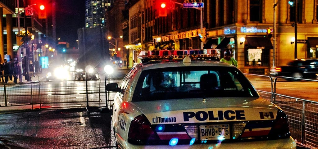 A Toronto police car blocks traffic on a busy city street at night.