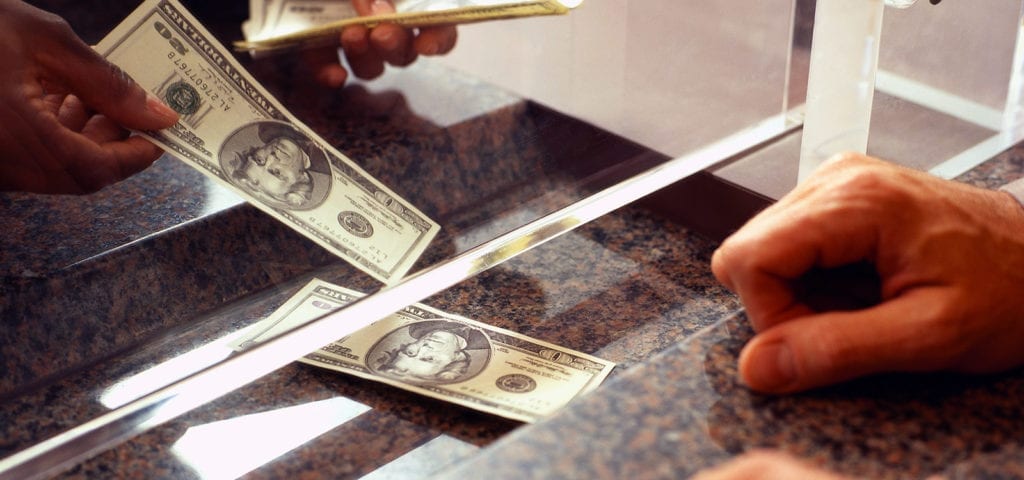 A bank teller counts out cash for their customer.