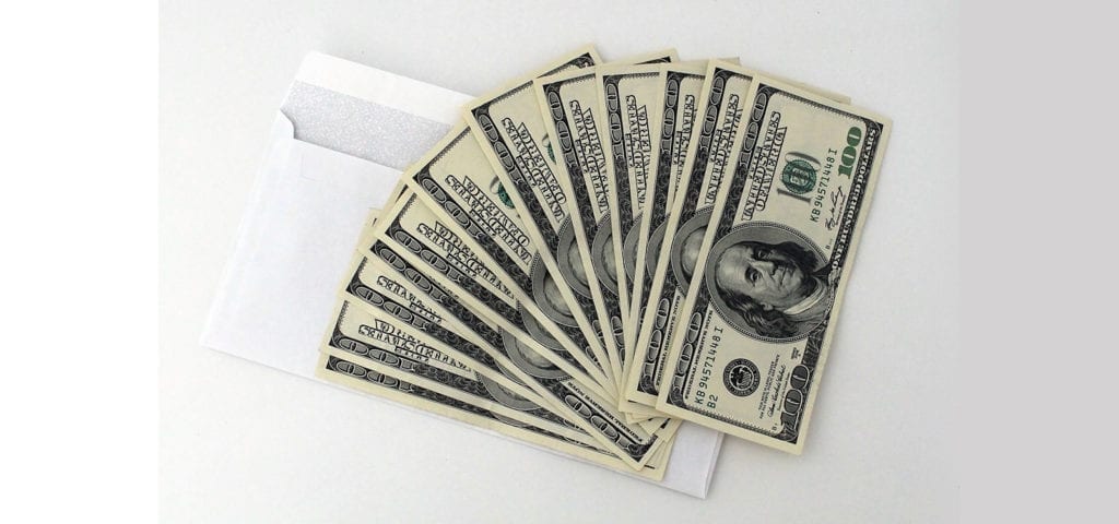 An envelope of hundred dollar bills sits on a white surface.