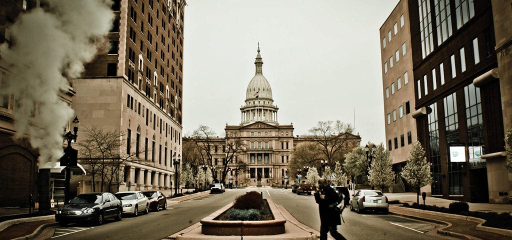 A photographer crosses the street in front of the Michigan State Capitol building in Lansing, Michigan.