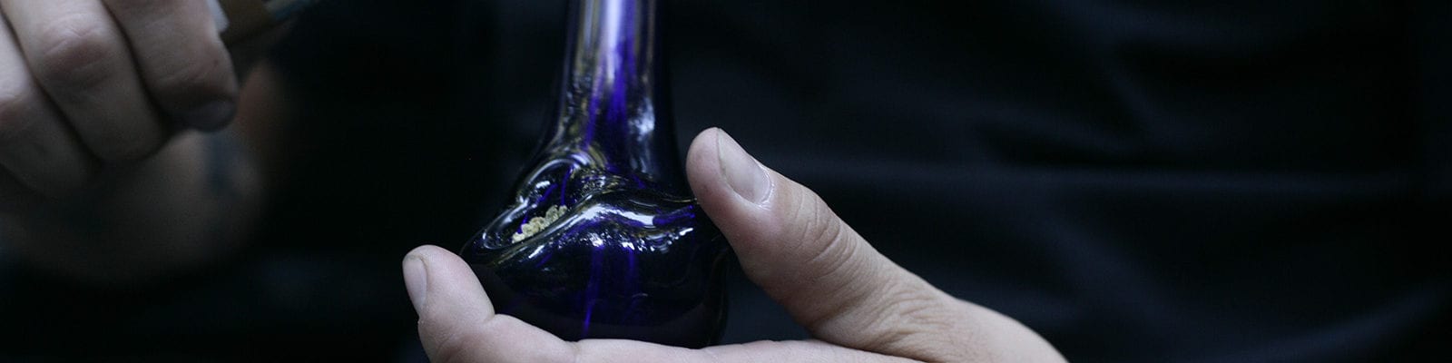 A man holds a lighter to a loaded bowl of ground cannabis.