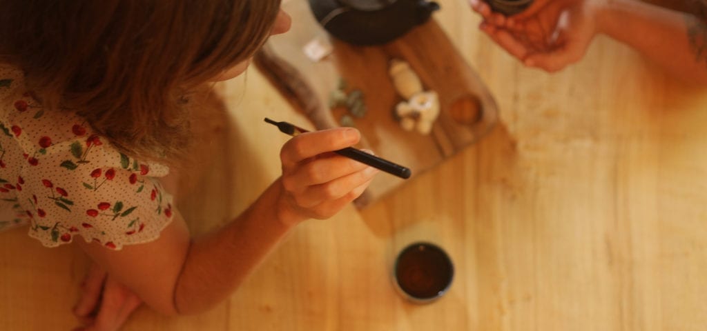 A woman uses a vape pen to consume CBD-rich cannabis oil in conjunction with hot cup of tea.