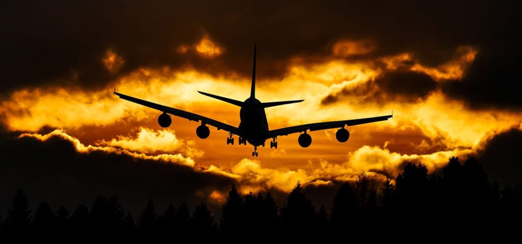 A commercial air plane flies in front of the glowing orange sky of sun down.
