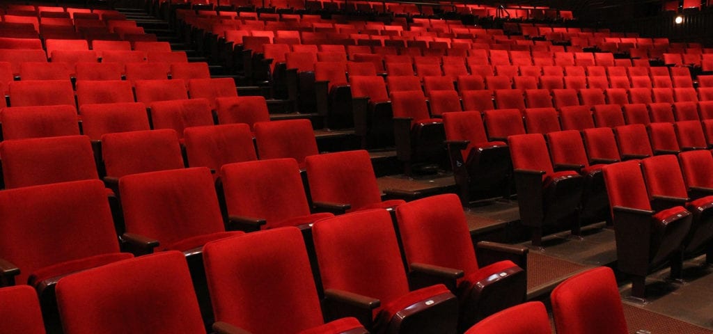 An empty auditorium with red folding cushioned chairs.