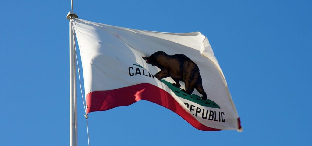 The state flag of California flying on a clear, blue skied day.
