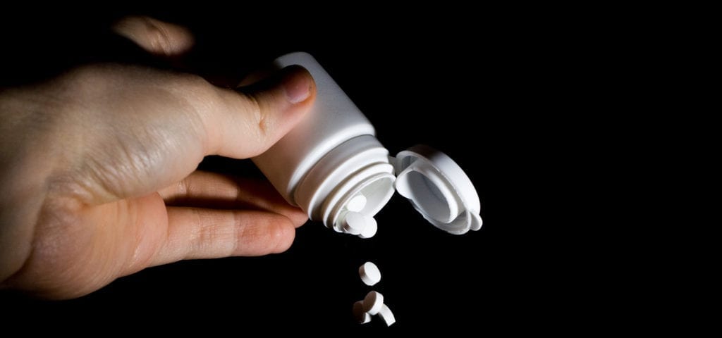 A person dumps pharmaceutical pills out of a pill bottle.