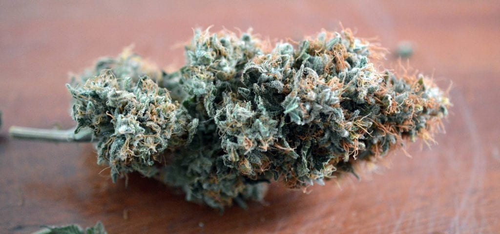 A cannabis nug lying on its side on top of a red-brown wood table.