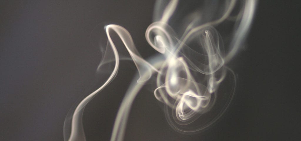 Smoke drifts upwards inside of a dark room.