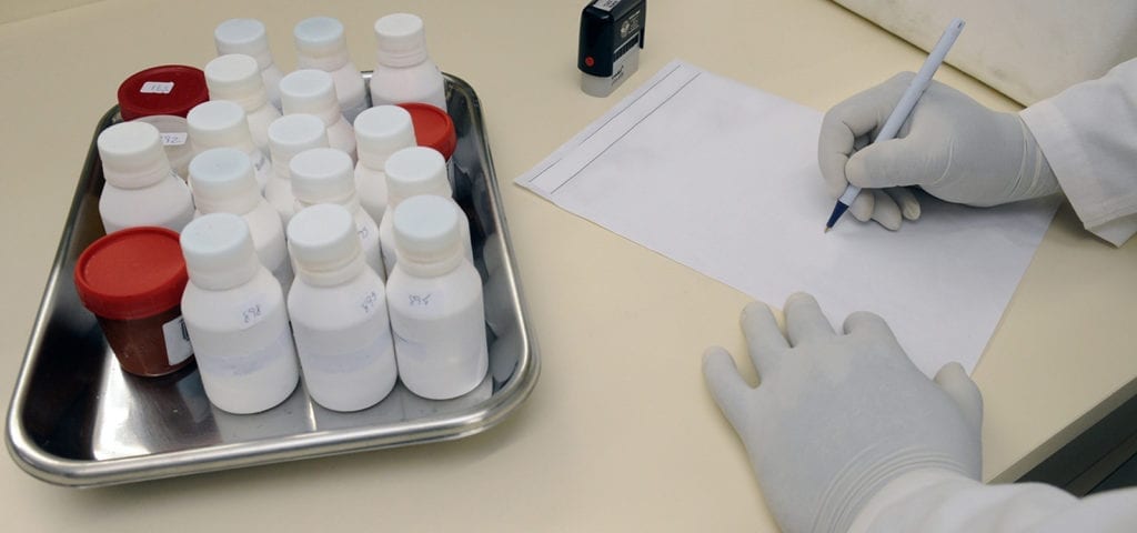 A person wearing a white glove writes on a paper next to some medicine bottles.