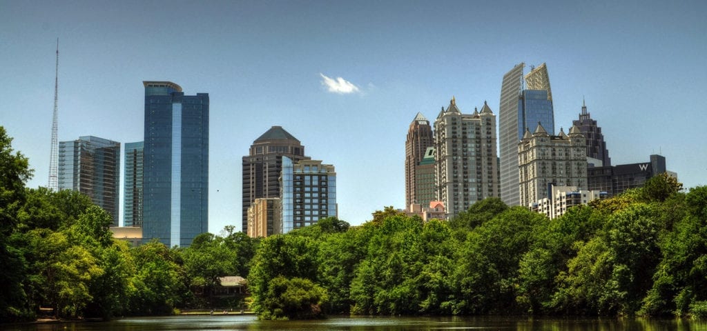 Photograph of Atlanta city poking above the treeline, pictured from a boat on a nearby lake.