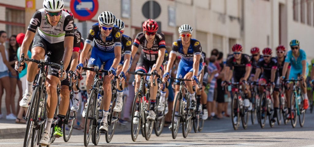 Professional bicycle athletes churn down the street in a large pack at the start of a race.