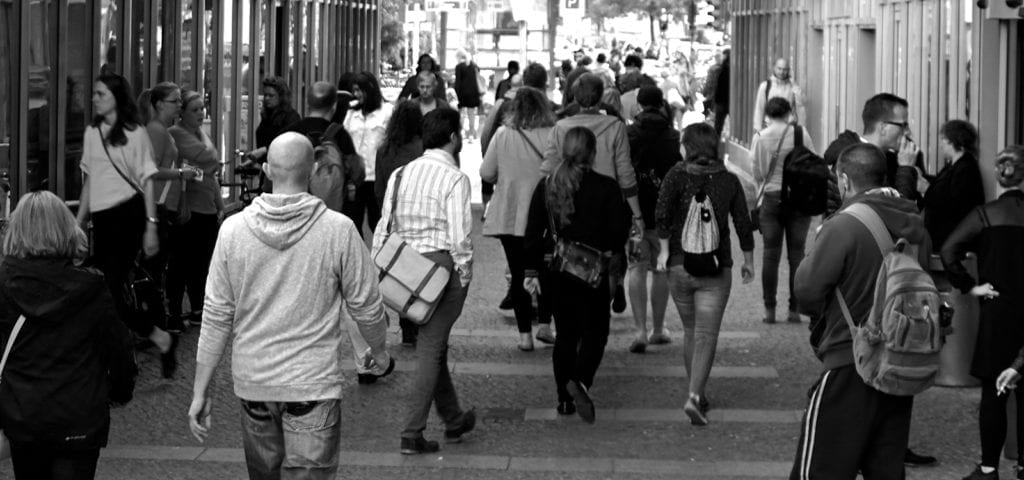 A black and white photograph of people milling down a street in a group.