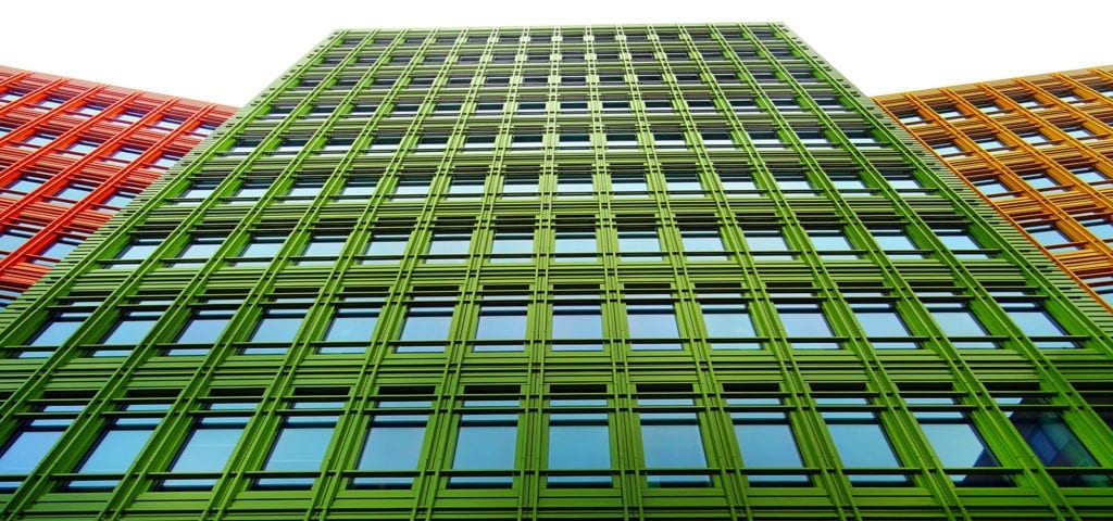 A tall, green building surrounded and contrasted by orange and red buildings.