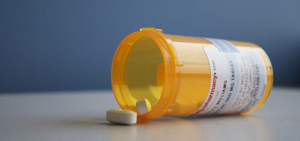 A mostly empty medicine pill bottle lies on its side on a white table with its cap removed.