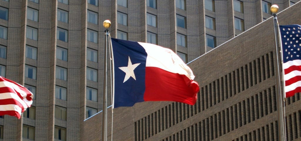 The Lone Star State's state flag flying between two U.S. flags at the Texas state capitol building.