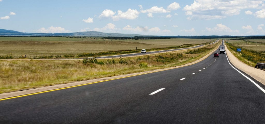 The open road of an interstate highway stretching between two pieces of farmland.