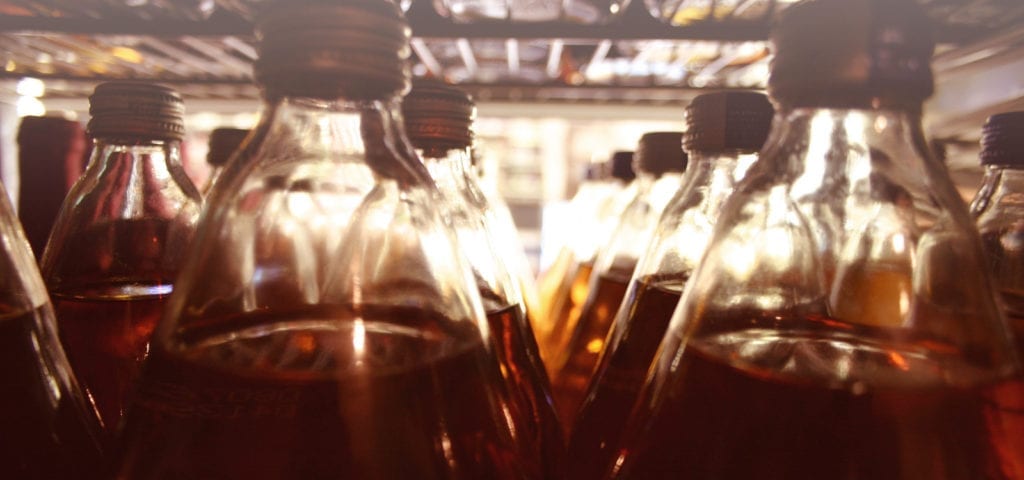 A camera looks out into a store's aisle from behind a shelf full of 40 oz. bottles of malt liquor.