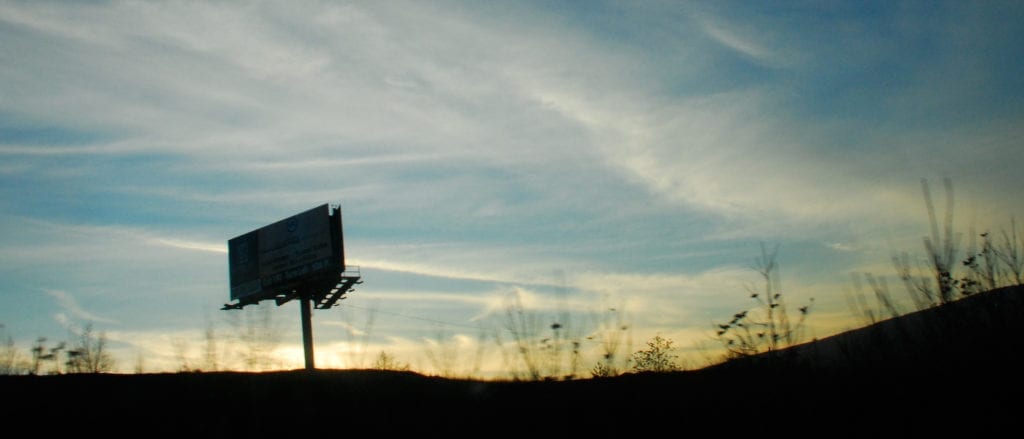 A lone billboard stands silhouetted against a California horizon.