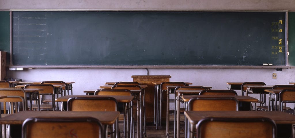 Wooden desks in a classroom in front of a black chalkboard.