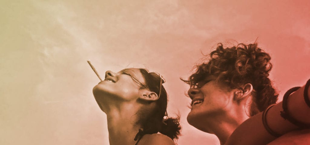 Two women, laughing, enjoy a smoke session outside.