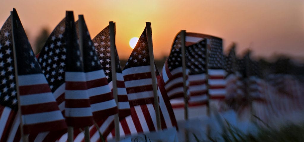 A sunset settling behind a row of small, toy American flags.