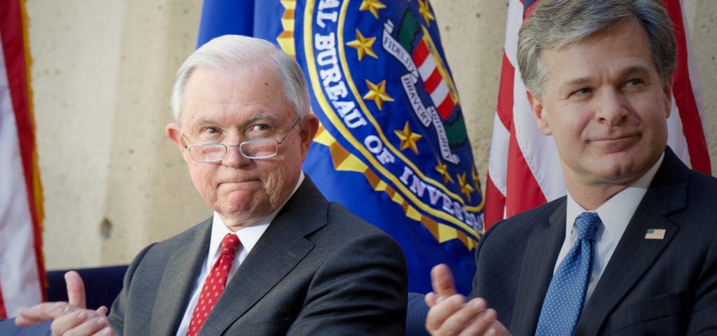 Grimacing Jeff Sessions sitting next to FBI director Christopher Wray.