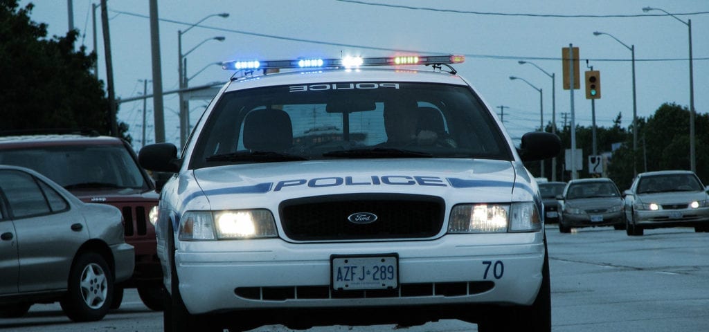 A blue-tinted photograph of a police car with its lights activated.