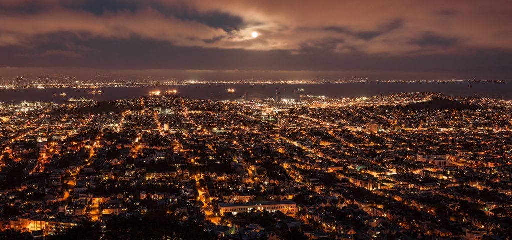 Nighttime view of the San Francisco sprawl with a full moon above it.