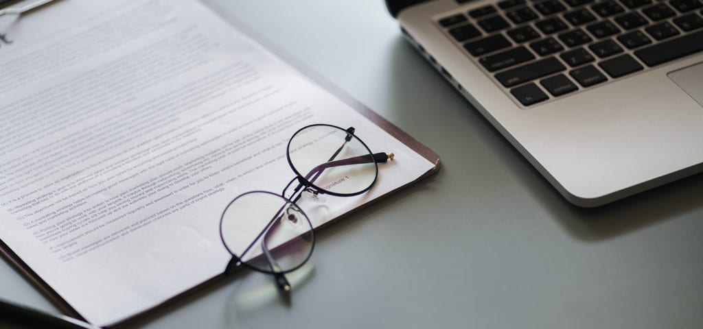 Flat photographic lay of a business concept — eyeglasses, paperwork, and a laptop computer.