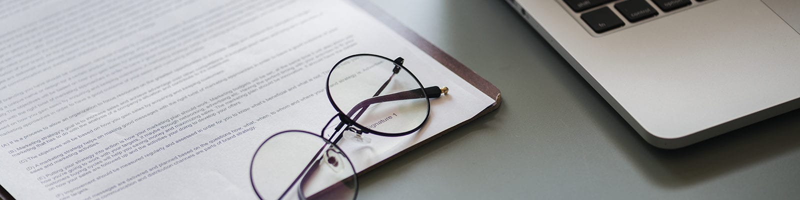 Flat photographic lay of a business concept — eyeglasses, paperwork, and a laptop computer.