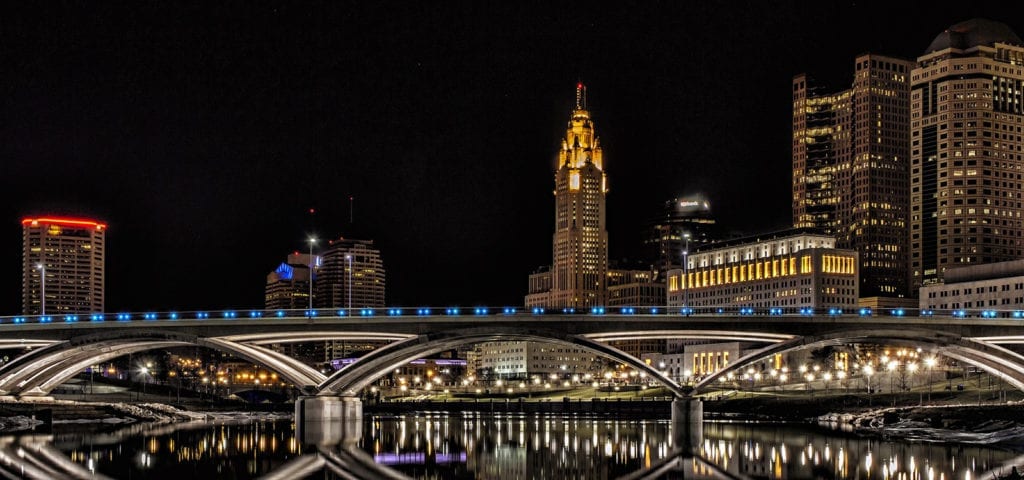 Nighttime photograph of a bridge in Columbus, Ohio with the city skyline behind it.